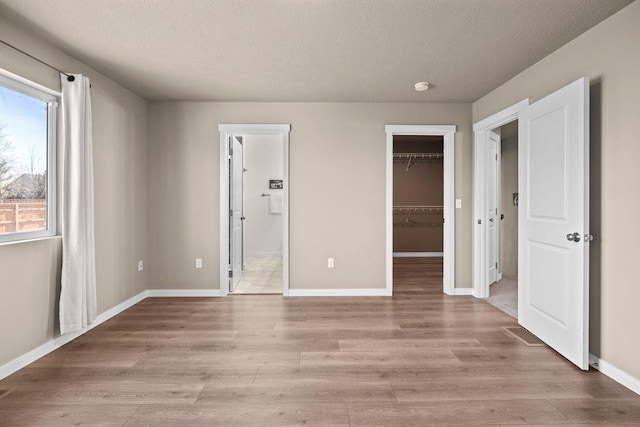 unfurnished bedroom featuring a textured ceiling, light wood finished floors, a walk in closet, and baseboards