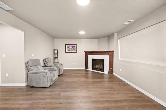 living area featuring visible vents, a fireplace, baseboards, and wood finished floors