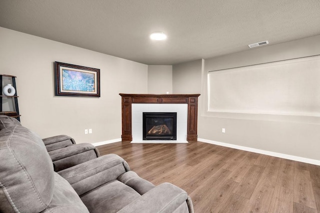 living area featuring visible vents, a tiled fireplace, a textured ceiling, wood finished floors, and baseboards