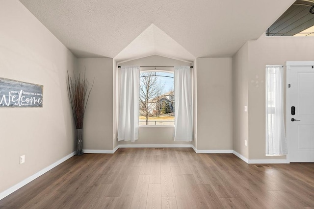 foyer entrance with vaulted ceiling, a textured ceiling, baseboards, and wood finished floors