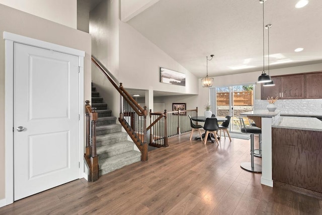 interior space featuring dark wood-style flooring, pendant lighting, decorative backsplash, high vaulted ceiling, and a kitchen breakfast bar