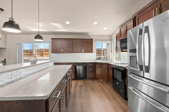 kitchen featuring a wealth of natural light, backsplash, black appliances, and wood finished floors