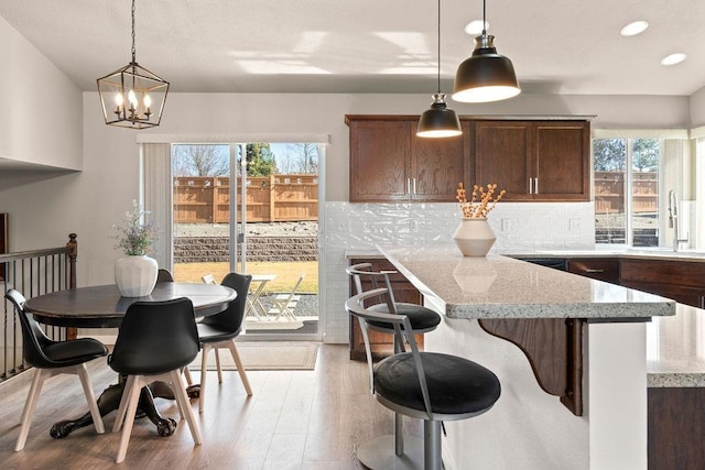 kitchen featuring light stone counters, pendant lighting, tasteful backsplash, a sink, and light wood-type flooring