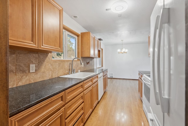 kitchen with white appliances, a sink, light wood-style floors, a chandelier, and backsplash