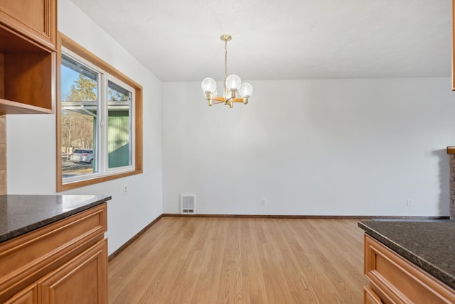 unfurnished dining area featuring baseboards, light wood-type flooring, visible vents, and a notable chandelier