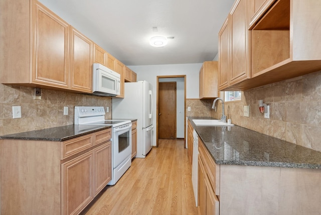 kitchen with white appliances, a sink, light wood-type flooring, decorative backsplash, and dark stone countertops