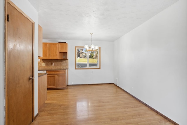 unfurnished dining area with a textured ceiling, light wood-type flooring, baseboards, and an inviting chandelier