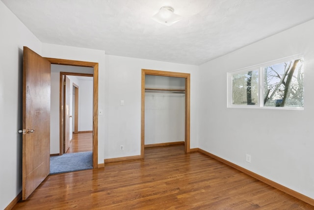 unfurnished bedroom with a closet, a textured ceiling, baseboards, and wood finished floors