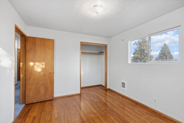 unfurnished bedroom featuring a closet, visible vents, baseboards, and wood finished floors