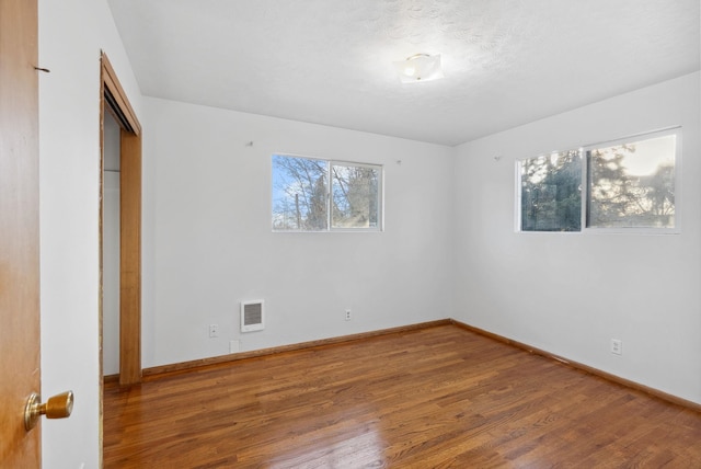 unfurnished bedroom with a closet, visible vents, a textured ceiling, wood finished floors, and baseboards