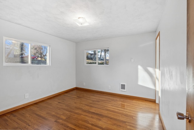 unfurnished room featuring visible vents, a textured ceiling, baseboards, and wood finished floors