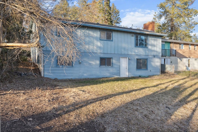 back of house with a chimney and a lawn