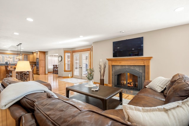 living area with french doors, recessed lighting, light wood-type flooring, a warm lit fireplace, and baseboards