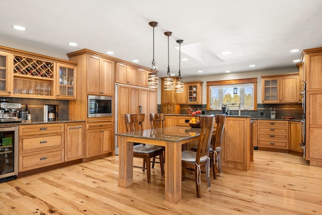 kitchen with beverage cooler, a kitchen island, a kitchen breakfast bar, built in appliances, and light wood-style floors