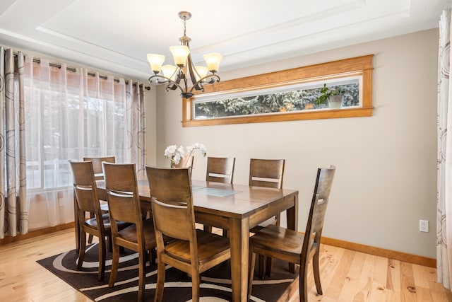 dining room featuring light wood-style flooring, baseboards, a raised ceiling, and a chandelier