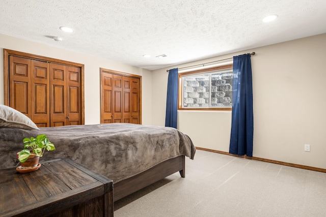 bedroom with a textured ceiling, recessed lighting, light colored carpet, baseboards, and multiple closets