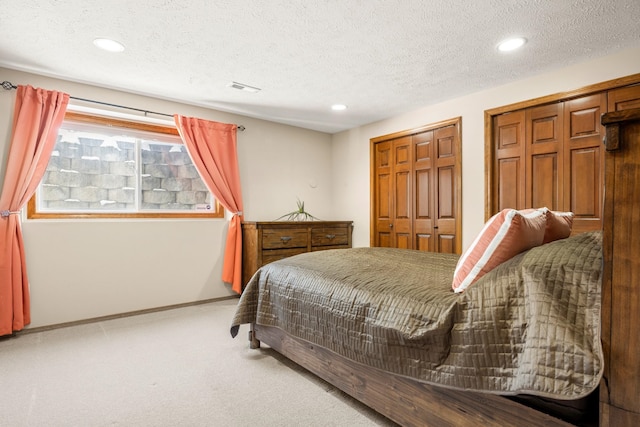 carpeted bedroom featuring baseboards, a textured ceiling, visible vents, and multiple closets