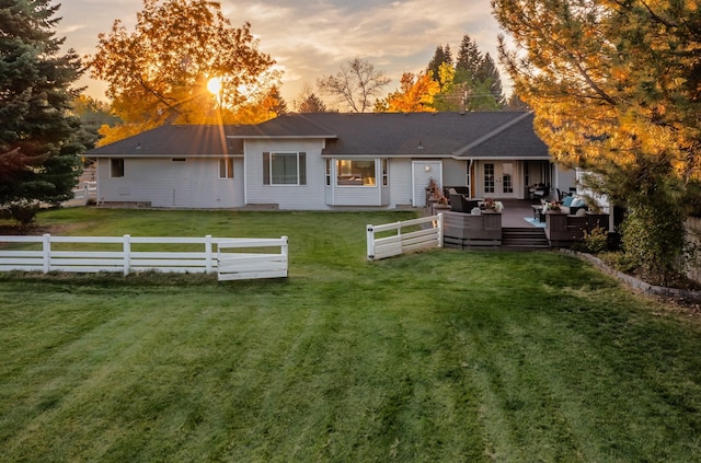 back of property at dusk featuring fence, a deck, a lawn, and french doors