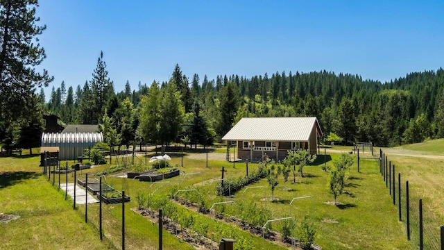 view of community featuring a yard, a wooded view, fence, and a garden