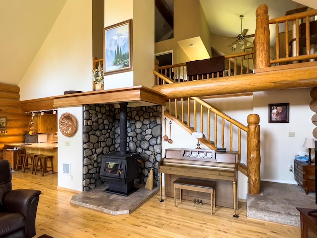 living room with high vaulted ceiling, rustic walls, wood finished floors, and a wood stove