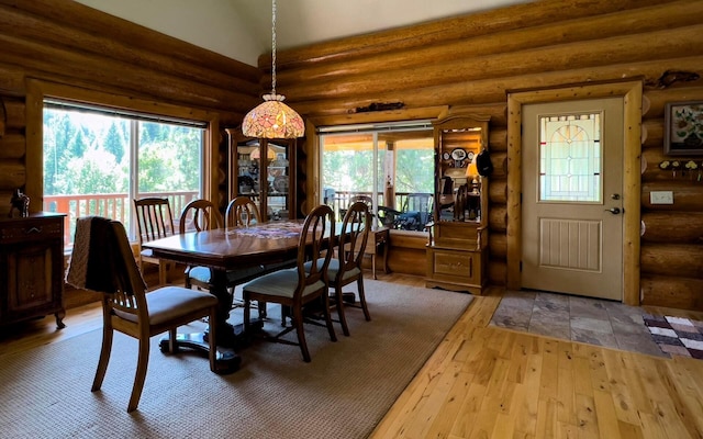 dining space with hardwood / wood-style flooring, log walls, and vaulted ceiling