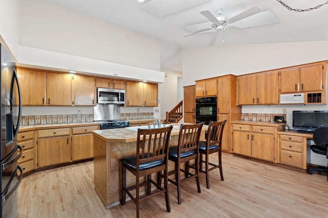 kitchen featuring tile counters, light wood-style flooring, ceiling fan, a kitchen breakfast bar, and black appliances