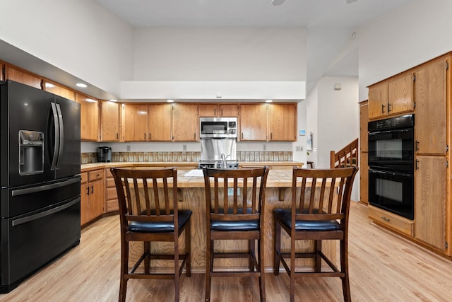 kitchen featuring a towering ceiling, black appliances, light wood-style flooring, and light countertops