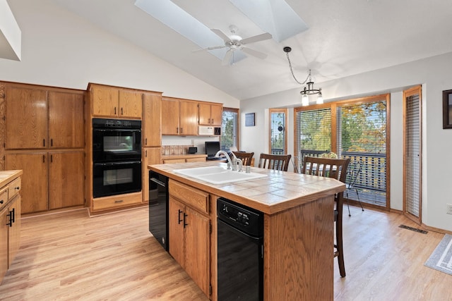 kitchen featuring light wood finished floors, tile countertops, black appliances, a kitchen bar, and a sink