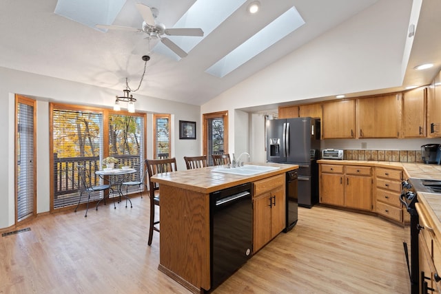 kitchen with a skylight, a sink, light wood-style floors, tile counters, and black appliances