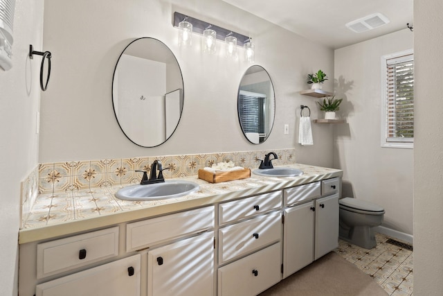 bathroom with toilet, double vanity, a sink, and visible vents