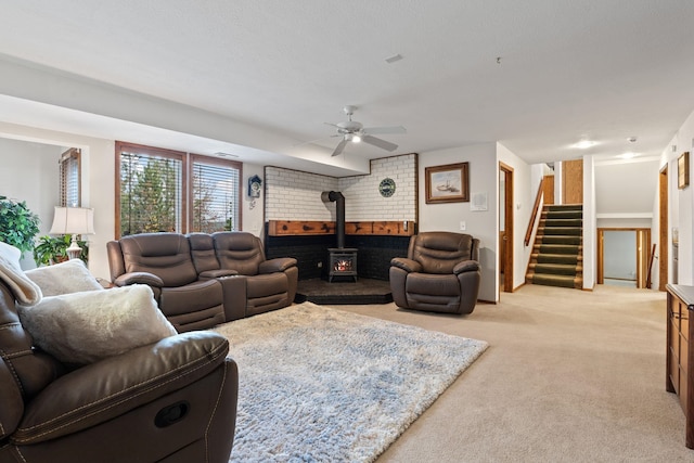 living room featuring a ceiling fan, a wood stove, light carpet, and stairs