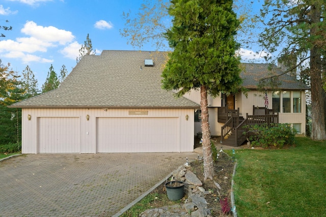 view of front facade featuring a shingled roof, decorative driveway, and a front lawn