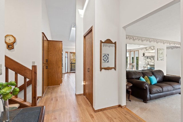 corridor with stairs, a high ceiling, light wood-style flooring, and baseboards