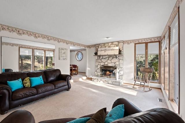 carpeted living area featuring a stone fireplace, visible vents, and a healthy amount of sunlight