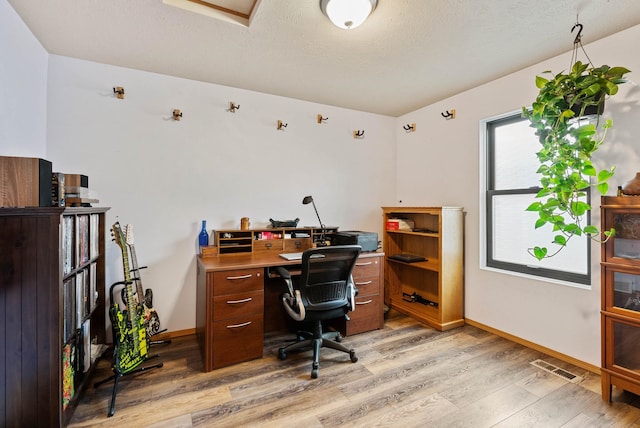 office space featuring light wood-style floors, visible vents, a textured ceiling, and baseboards