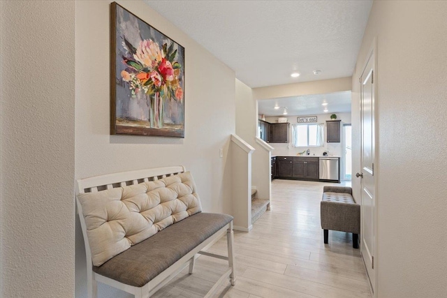 corridor featuring baseboards, a textured wall, light wood finished floors, and stairs