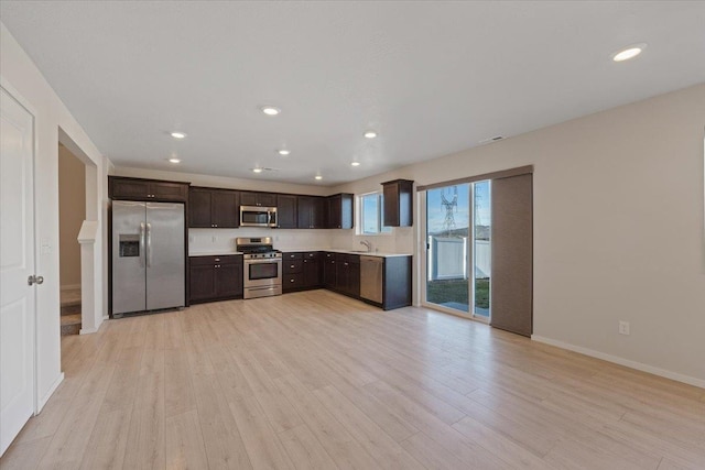 kitchen with stainless steel appliances, light countertops, light wood-style floors, a sink, and dark brown cabinets