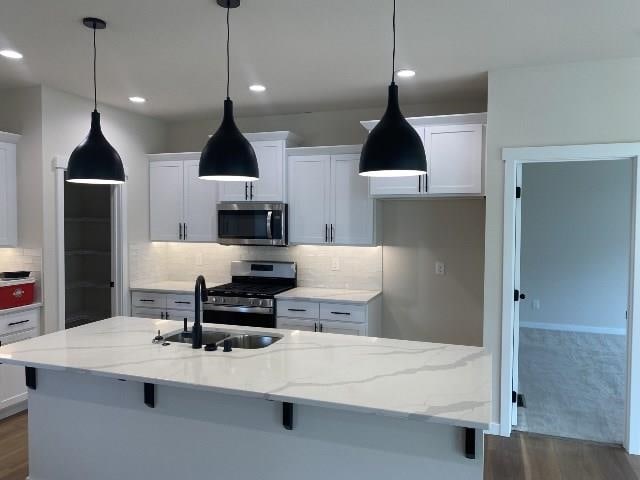 kitchen featuring stainless steel appliances, dark wood-style flooring, a sink, tasteful backsplash, and a center island with sink