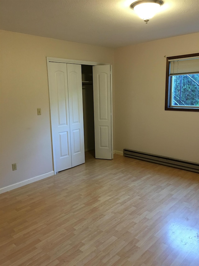 unfurnished bedroom with light wood-type flooring, a baseboard radiator, baseboards, and a closet