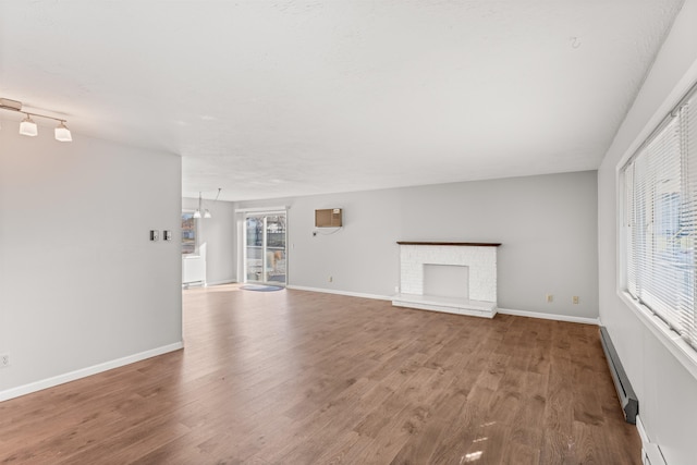 unfurnished living room featuring a baseboard radiator, a fireplace, baseboards, and wood finished floors