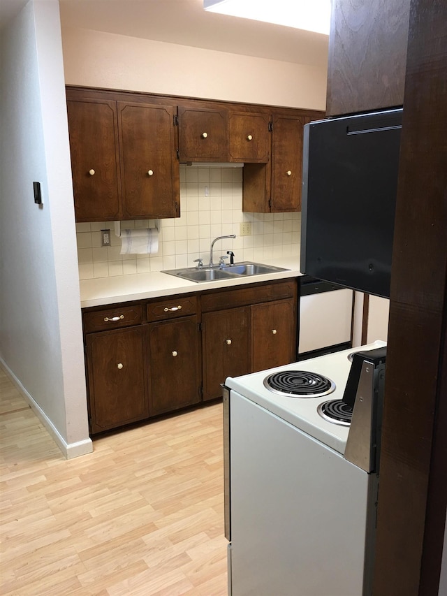 kitchen featuring electric stove, a sink, light wood-style flooring, and decorative backsplash