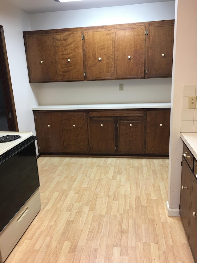 kitchen featuring light countertops, white electric range, dark brown cabinets, and light wood finished floors