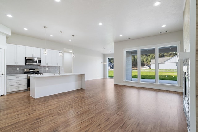 kitchen featuring tasteful backsplash, white cabinets, appliances with stainless steel finishes, open floor plan, and wood finished floors