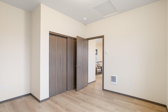 unfurnished bedroom with attic access, baseboards, visible vents, light wood-style flooring, and a closet