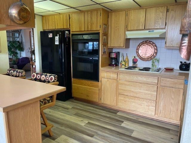 kitchen with black appliances, light countertops, light wood-style flooring, and under cabinet range hood