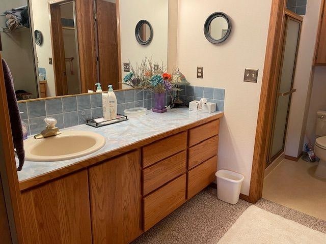 bathroom featuring a stall shower, toilet, vanity, and decorative backsplash