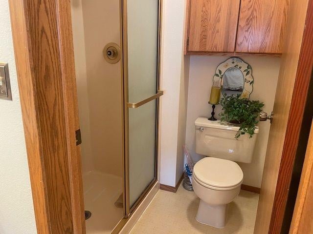 bathroom with a stall shower, baseboards, and toilet