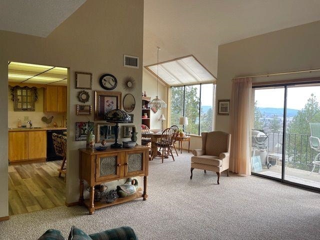 living area featuring high vaulted ceiling, visible vents, and light colored carpet