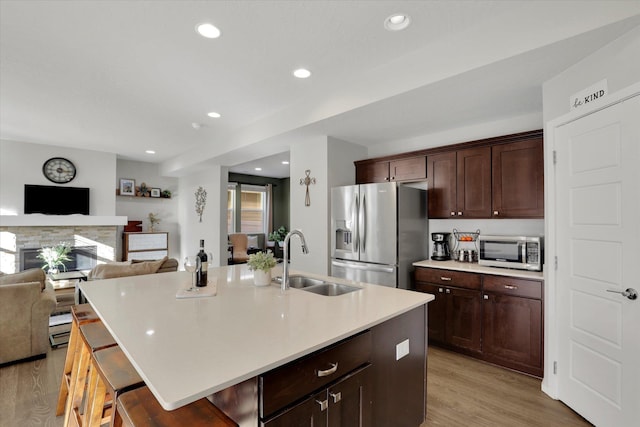 kitchen with light wood finished floors, open floor plan, stainless steel appliances, a fireplace, and a sink