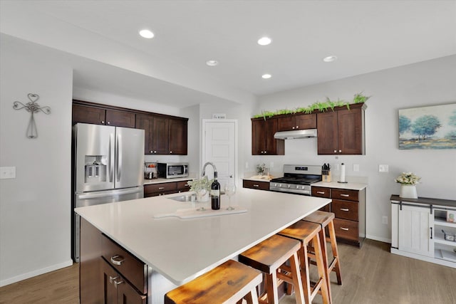 kitchen featuring stainless steel appliances, a sink, wood finished floors, under cabinet range hood, and a kitchen breakfast bar